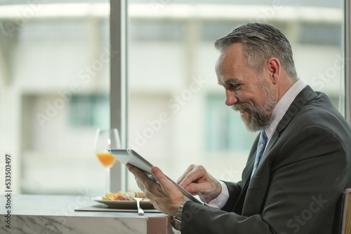 Caucasian Businessman using tablet computer. Happy middle aged man sitting in a restaurant. Entrepreneur working online, reading finance report, thinking.
