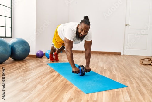 Young african american man smiling confident training abs exercise using roller at sport center