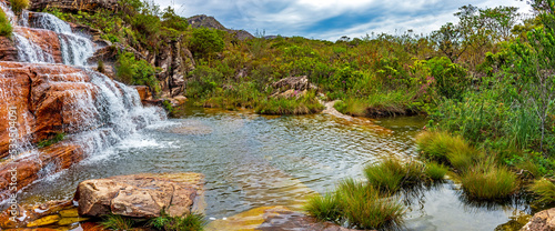 Panoramic view of waterfall and lake among the vegetation with mountains in background on Biribiri environmental reserve on Diamantina, Minas Gerais state, Brazil.
