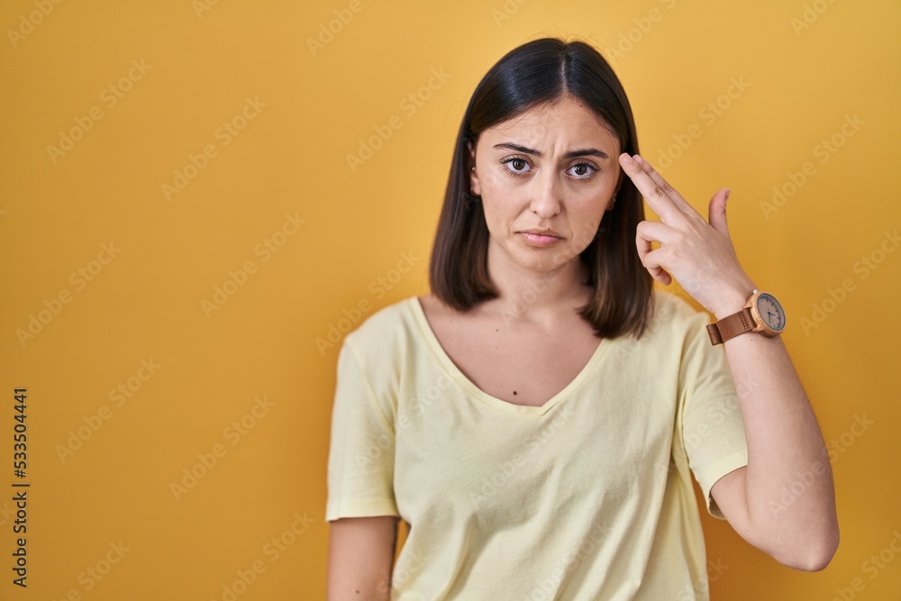 Hispanic girl wearing casual t shirt over yellow background shooting and killing oneself pointing hand and fingers to head like gun, suicide gesture. Hispanic girl wearing casual t shirt over yellow background shooting and killing oneself pointing hand and fingers to head like gun, suicide gesture.