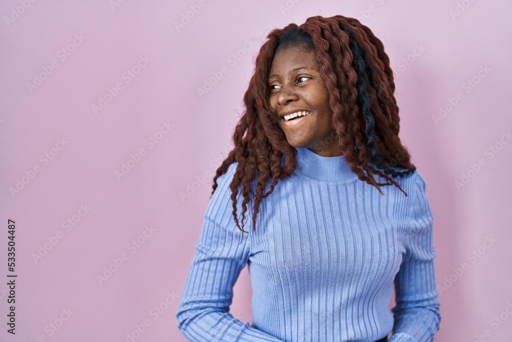 African woman standing over pink background looking away to side with smile on face, natural expression. laughing confident. African woman standing over pink background looking away to side with smile on face, natural expression. laughing confident.