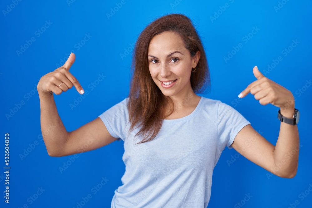 Brunette woman standing over blue background looking confident with smile on face, pointing oneself with fingers proud and happy. Brunette woman standing over blue background looking confident with smile on face, pointing oneself with fingers proud and happy.