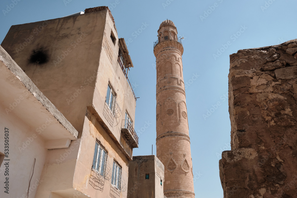 Grand mosque of Mardin and narrow old town street. Bottom up view of Ulu Cami minaret against blue sky in sunny afternoon. Mardin, Turkey