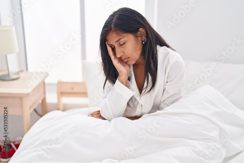 Young beautiful hispanic woman tired sitting on bed at bedroom