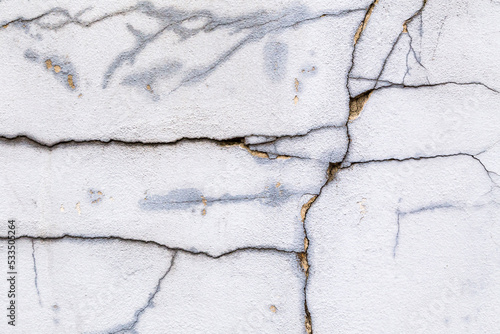 Textured grey white, concrete wall with cracks and grungy, rough painted, detail. Design element abstract background with holes, many paint patches and scratches.
