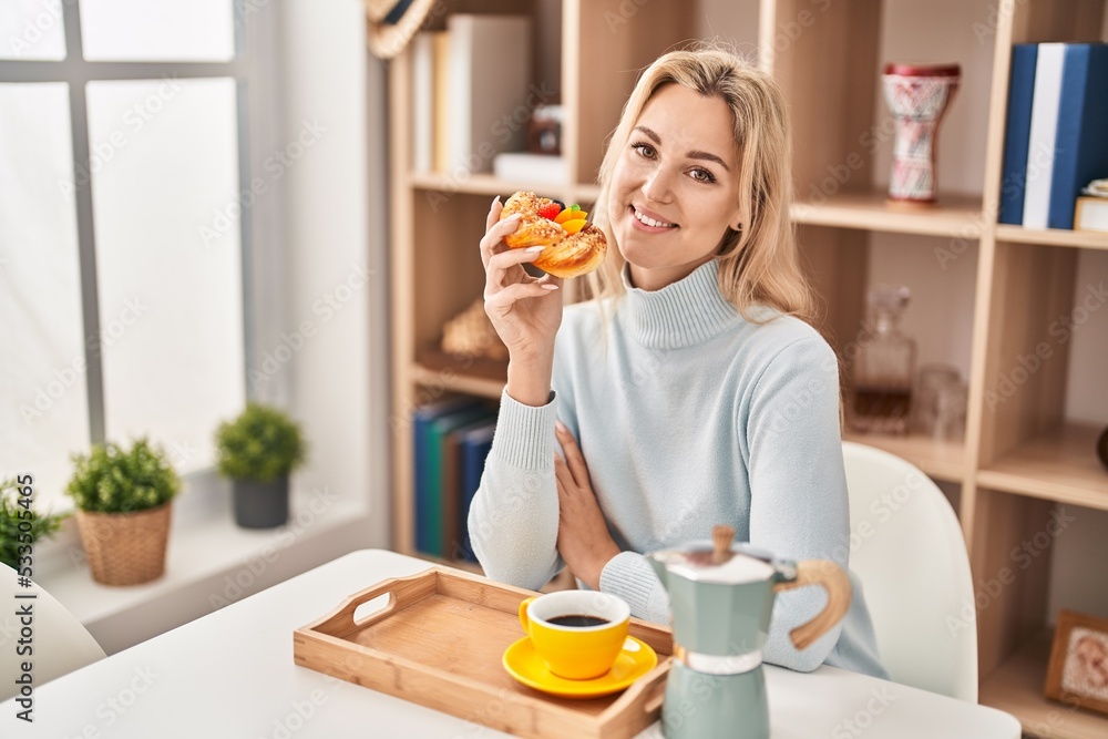 Young blonde woman having breakfast sitting on table at home Young blonde woman having breakfast sitting on table at home
