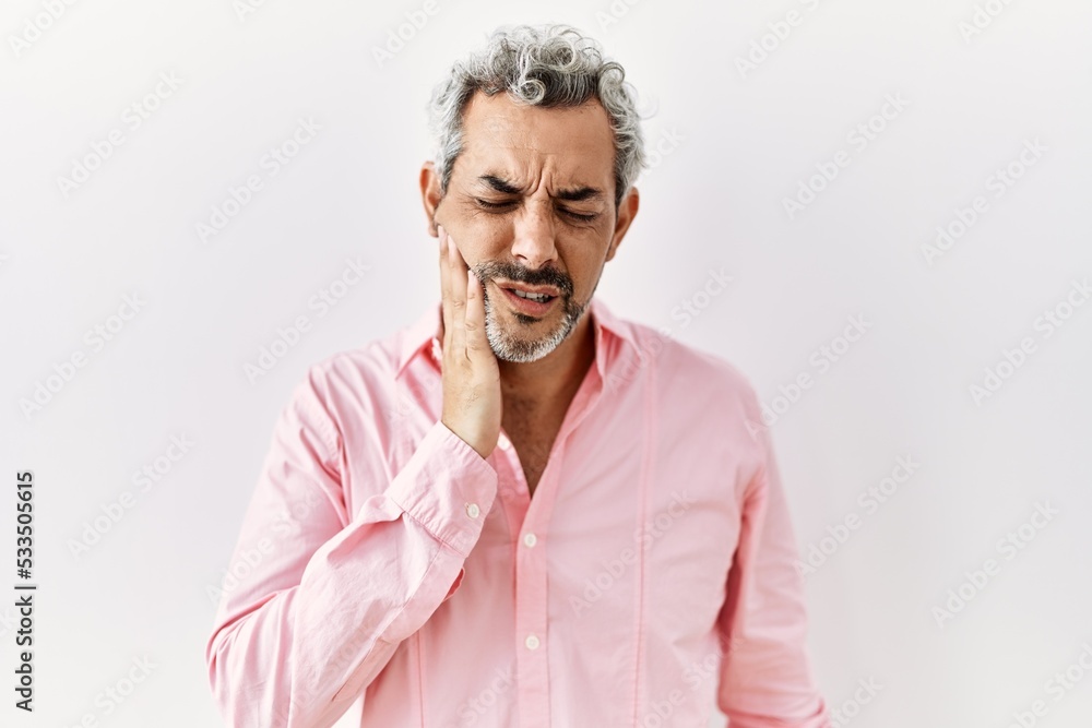 Obraz premium Middle age hispanic man standing over isolated background touching mouth with hand with painful expression because of toothache or dental illness on teeth. dentist