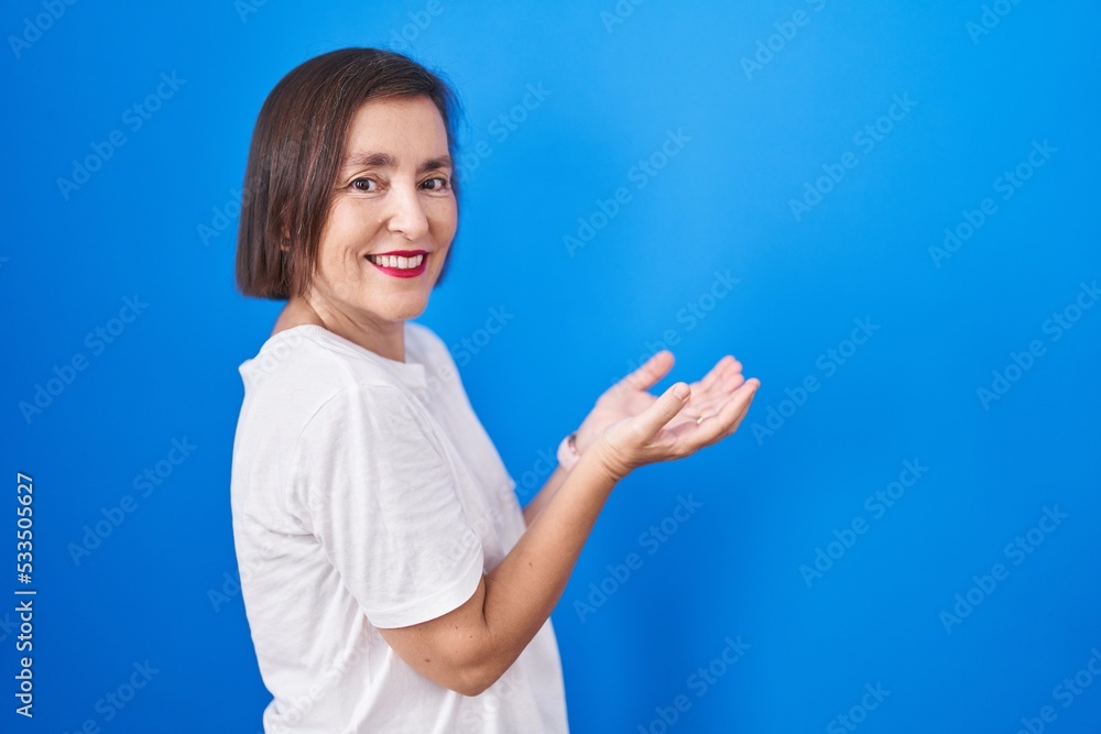 Middle age hispanic woman standing over blue background pointing aside with hands open palms showing copy space, presenting advertisement smiling excited happy Middle age hispanic woman standing over blue background pointing aside with hands open palms showing copy space, presenting advertisement smiling excited happy