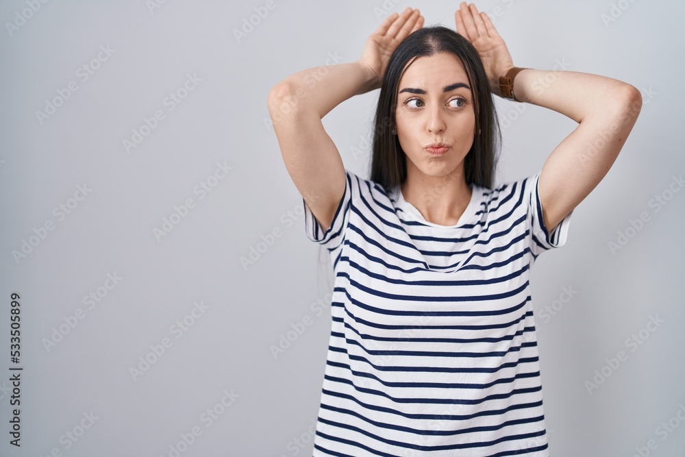 Young brunette woman wearing striped t shirt doing bunny ears gesture with hands palms looking cynical and skeptical. easter rabbit concept. Young brunette woman wearing striped t shirt doing bunny ears gesture with hands palms looking cynical and skeptical. easter rabbit concept.