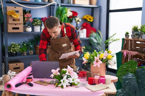 Young caucasian man florist using laptop reading document at flower shop