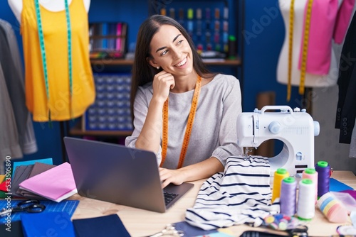 Young beautiful hispanic woman tailor smiling confident using laptop at clothing factory
