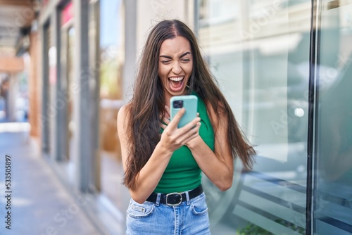 Wallpaper Mural Young beautiful hispanic woman using smartphone with surprise expression at street Torontodigital.ca