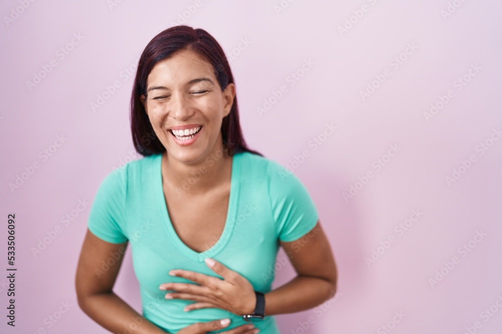 Young hispanic woman standing over pink background smiling and laughing hard out loud because funny crazy joke with hands on body. Young hispanic woman standing over pink background smiling and laughing hard out loud because funny crazy joke with hands on body.