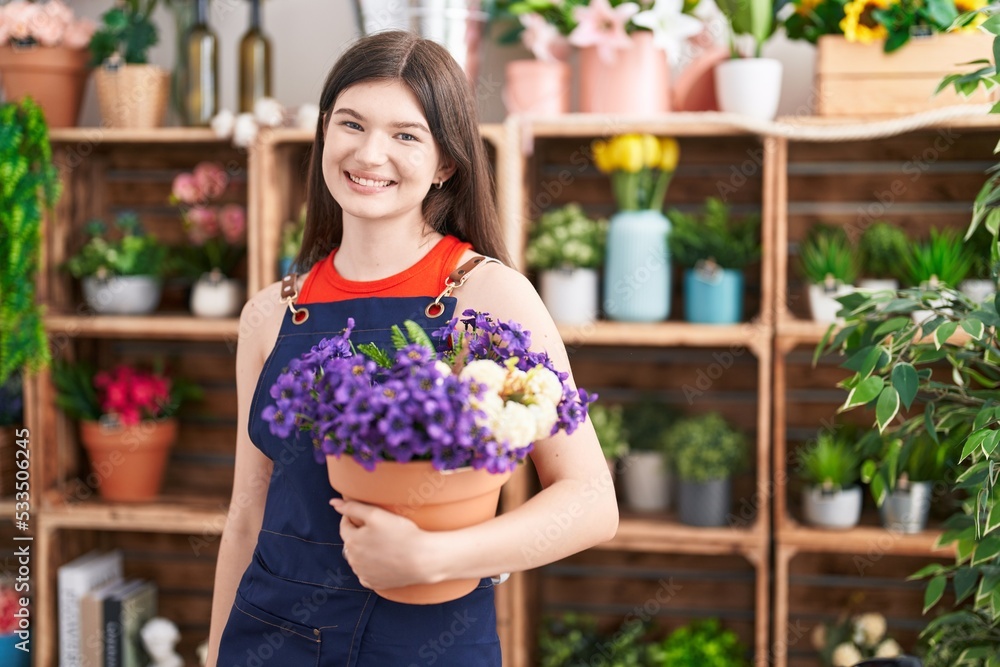 Young caucasian woman working at florist shop holding pot with flowers looking positive and happy standing and smiling with a confident smile showing teeth