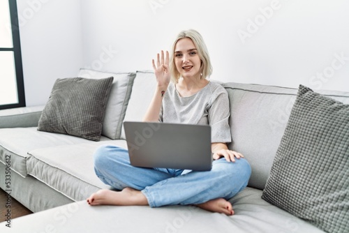 Young caucasian woman using laptop at home sitting on the sofa showing and pointing up with fingers number four while smiling confident and happy.