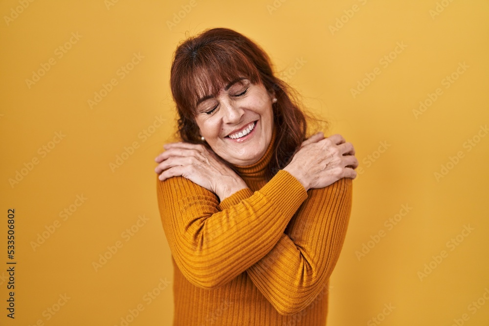 Middle age hispanic woman standing over yellow background hugging oneself happy and positive, smiling confident. self love and self care Middle age hispanic woman standing over yellow background hugging oneself happy and positive, smiling confident. self love and self care