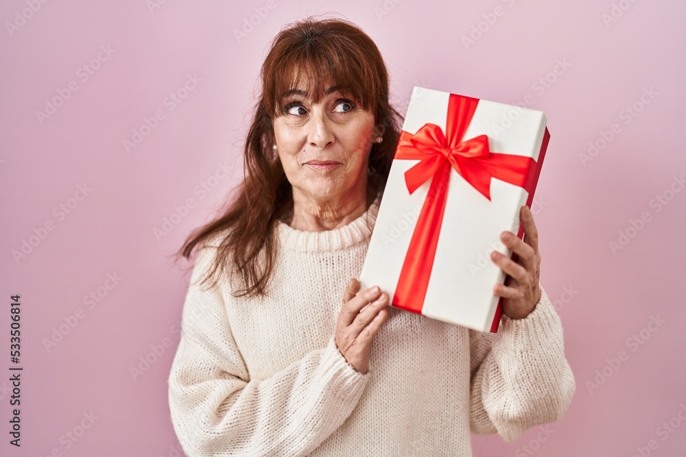 Middle age hispanic woman holding present smiling looking to the side and staring away thinking. Middle age hispanic woman holding present smiling looking to the side and staring away thinking.