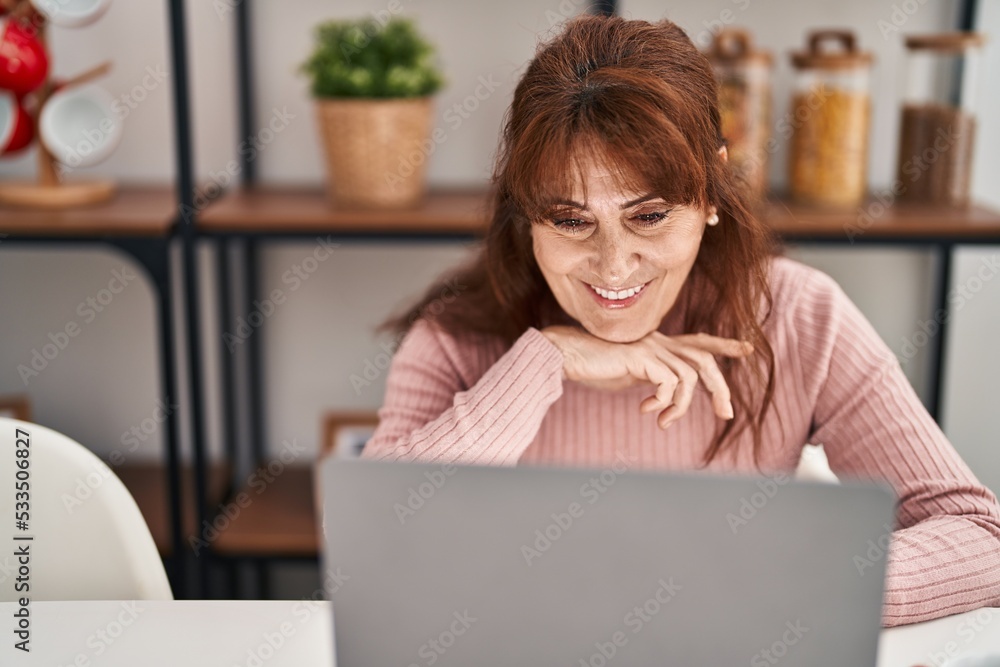 Middle age woman using laptop sitting on table at home Middle age woman using laptop sitting on table at home
