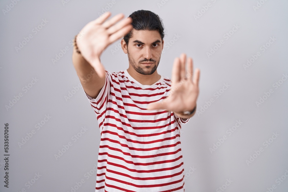 Fototapeta premium Hispanic man with long hair standing over isolated background doing frame using hands palms and fingers, camera perspective