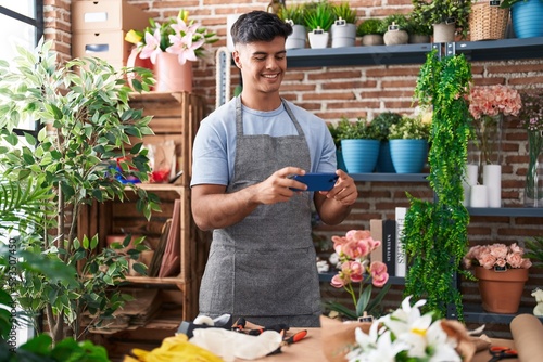 Young hispanic man florist make photo to plant by smartphone at flower shop