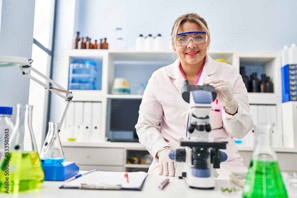 Young hispanic woman wearing scientist uniform using microscope at laboratory Young hispanic woman wearing scientist uniform using microscope at laboratory