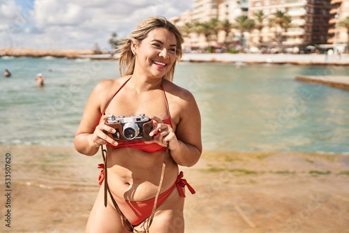 Young hispanic woman wearing bikini using vintage camera at seaside © Krakenimages.com