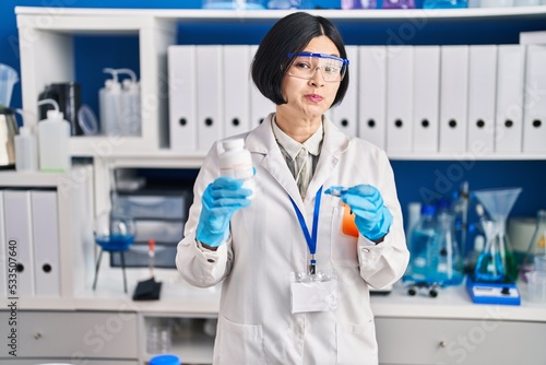 Young asian woman working at scientist laboratory smiling looking to the side and staring away thinking.