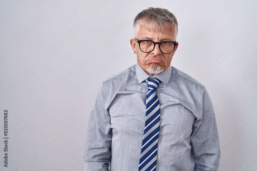 Hispanic business man with grey hair wearing glasses depressed and worry for distress, crying angry and afraid. sad expression. Hispanic business man with grey hair wearing glasses depressed and worry for distress, crying angry and afraid. sad expression.