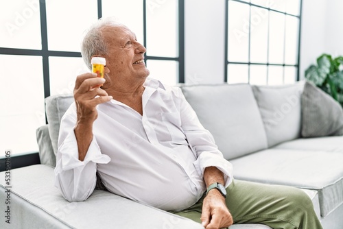 Senior man holding pills looking away to side with smile on face, natural expression. laughing confident.