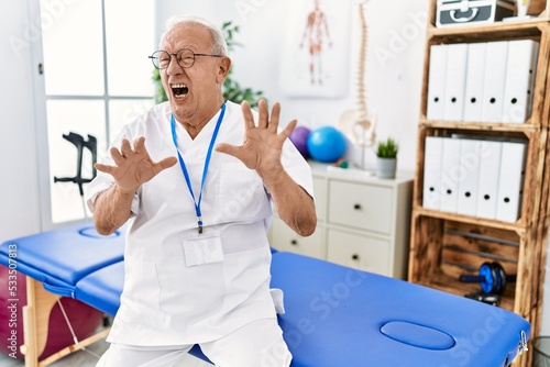 Senior physiotherapy man working at pain recovery clinic afraid and terrified with fear expression stop gesture with hands  shouting in shock. panic concept.