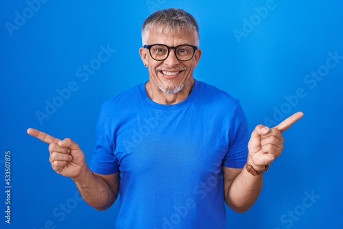 Hispanic man with grey hair standing over blue background smiling confident pointing with fingers to different directions. copy space for advertisement