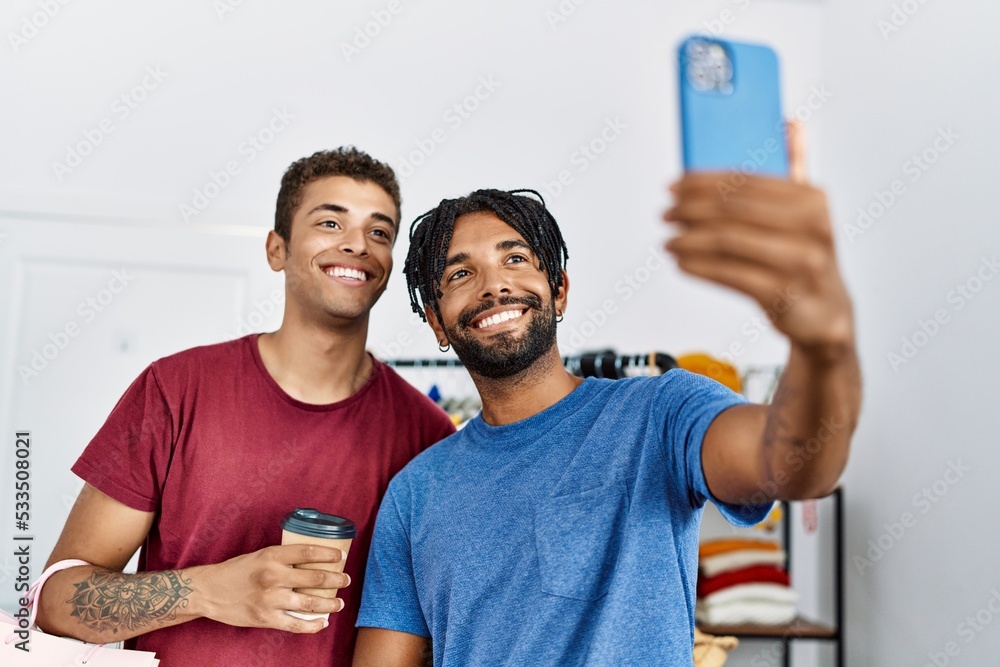 Two men friends holding shopping bags make selfie by the smartphone at clothing store