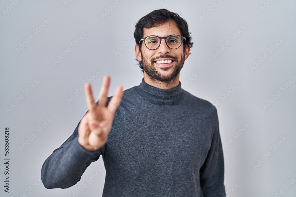 Handsome latin man standing over isolated background showing and pointing up with fingers number three while smiling confident and happy. Handsome latin man standing over isolated background showing and pointing up with fingers number three while smiling confident and happy.