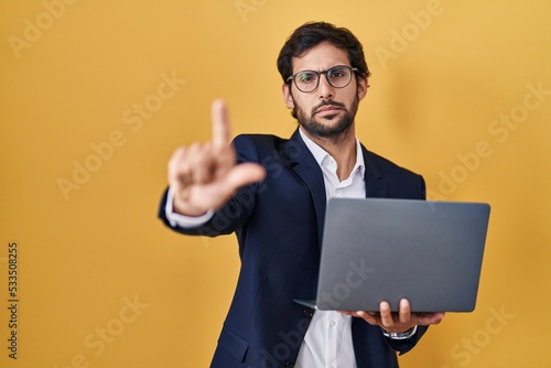 Handsome latin man working using computer laptop pointing with finger up and angry expression, showing no gesture