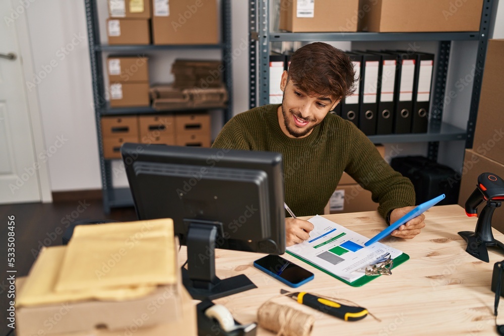 Young arab man ecommerce business worker writing on document using touchpad at office