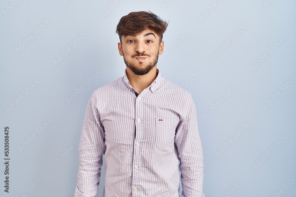 Arab man with beard standing over blue background puffing cheeks with funny face. mouth inflated with air, crazy expression. Arab man with beard standing over blue background puffing cheeks with funny face. mouth inflated with air, crazy expression.