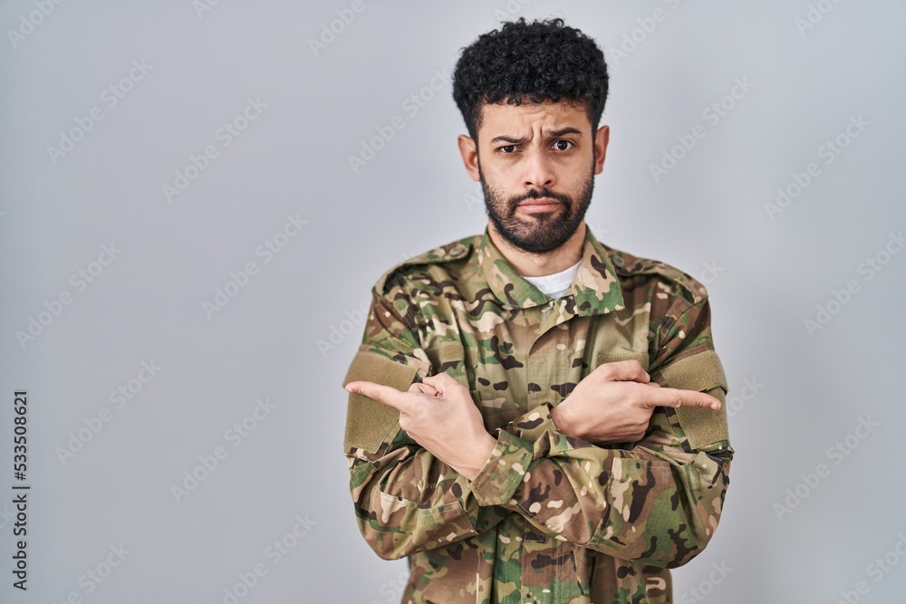 Arab man wearing camouflage army uniform pointing to both sides with fingers, different direction disagree Arab man wearing camouflage army uniform pointing to both sides with fingers, different direction disagree