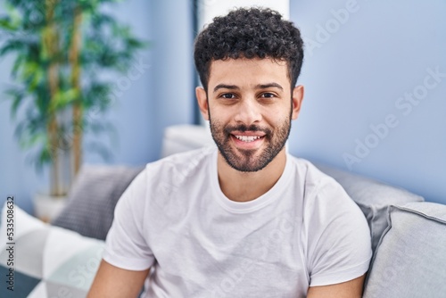 Young arab man smiling confident sitting on sofa at home