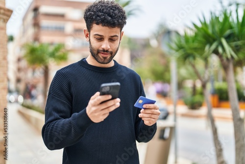 Young arab man using smartphone and credit card at street