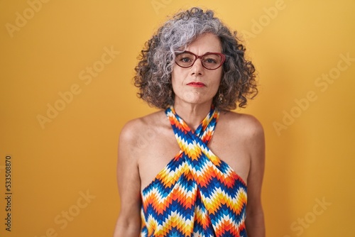 Εκτύπωση καμβά Middle age woman with grey hair standing over yellow background relaxed with serious expression on face