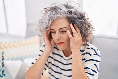 Middle age grey-haired woman suffering for headache sitting on sofa at home