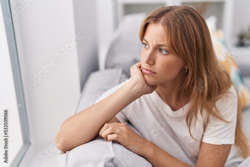 Young blonde girl sitting on sofa with serious expression at home