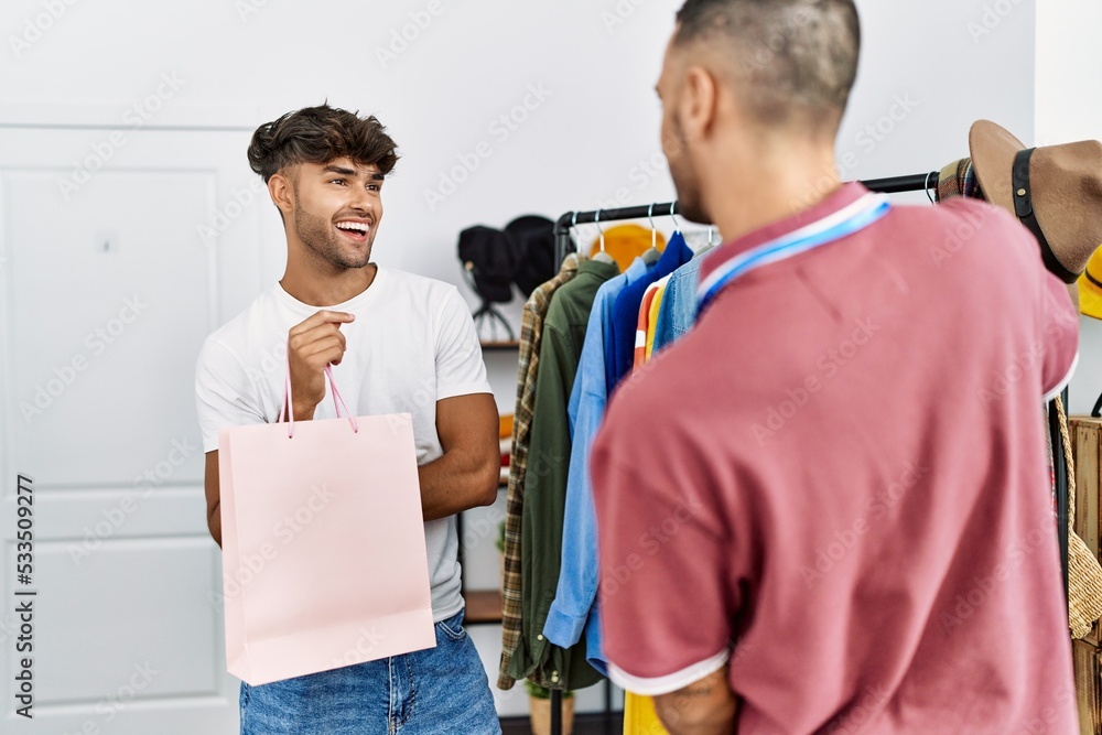 Young hispanic shopkeeper showing clothes to customer at clothing store. Young hispanic shopkeeper showing clothes to customer at clothing store.