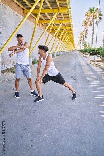 Two hispanic men couple smiling confident stretching at street