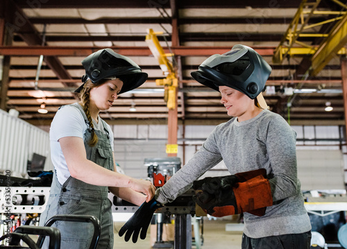 a female welder helps child welder who is a student get on welding gloves and other ppe photo