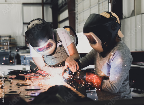 Industrial woman welder teaches younger student how to MIG weld metal with a torch photo