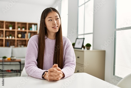 Young chinese girl smiling happy sitting on the table at home.