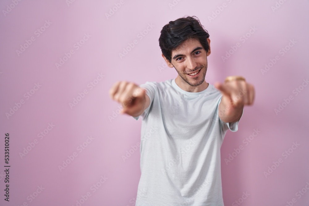 Young hispanic man standing over pink background pointing to you and the camera with fingers, smiling positive and cheerful Young hispanic man standing over pink background pointing to you and the camera with fingers, smiling positive and cheerful