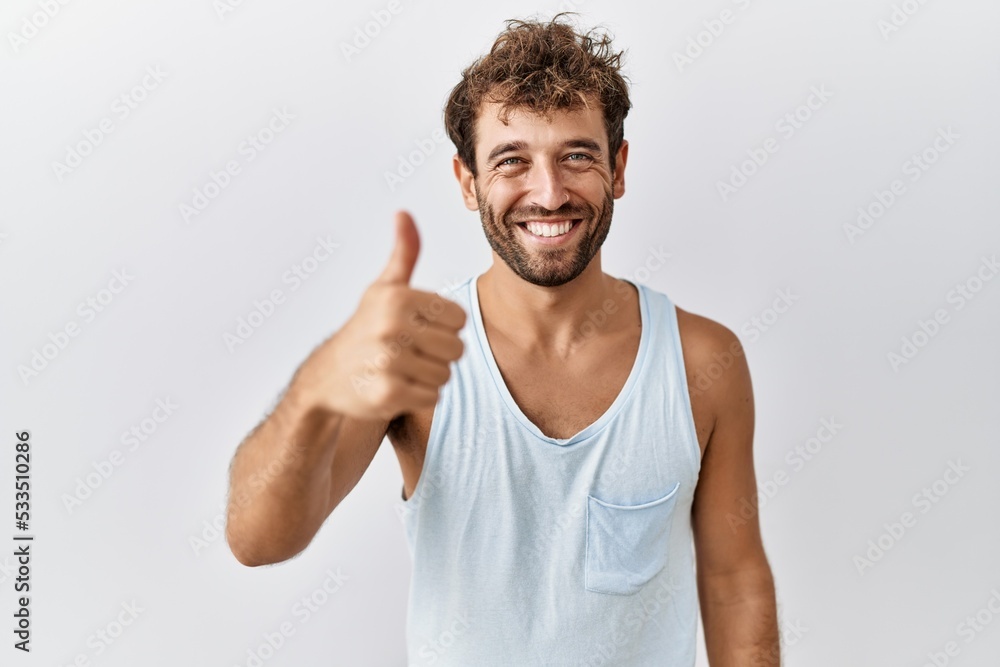Young handsome man standing over isolated background doing happy thumbs up gesture with hand. approving expression looking at the camera showing success. Young handsome man standing over isolated background doing happy thumbs up gesture with hand. approving expression looking at the camera showing success.