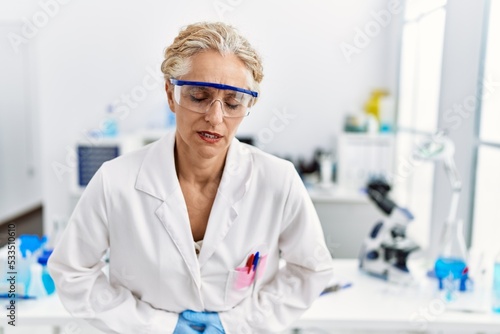 Middle age blonde woman working at scientist laboratory with hand on stomach because indigestion  painful illness feeling unwell. ache concept.